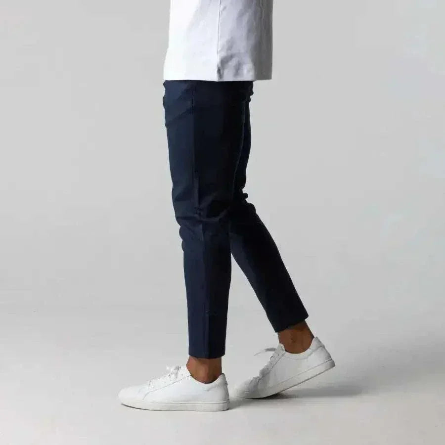 A man wearing navy slim fit golf trousers from GolfThing and white sneakers on a plain background