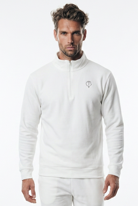 A man modeling a white long-sleeve quarter-zip golf jumper and matching white jogger pants with white sneakers, photographed against a seamless white studio background.