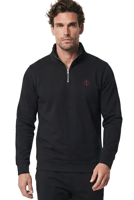A man modeling a black long-sleeve quarter-zip golf sweater with a small embroidered logo on the left chest, paired with black pants and black shoes, against a plain white studio background.