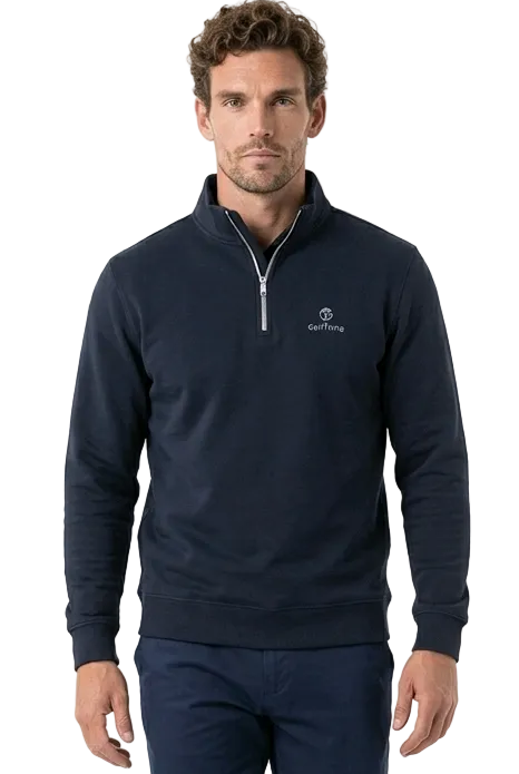 A man modeling a navy blue quarter-zip golf jumper and matching navy golf trousers with white golf trainers, photographed against a clean white studio background.