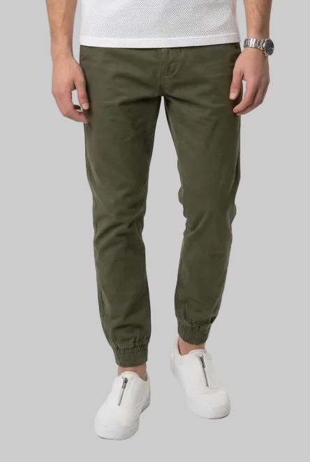 A man modeling a white long-sleeve crewneck shirt, olive green cuffed golf trousers, and white sneakers against a plain white studio background.