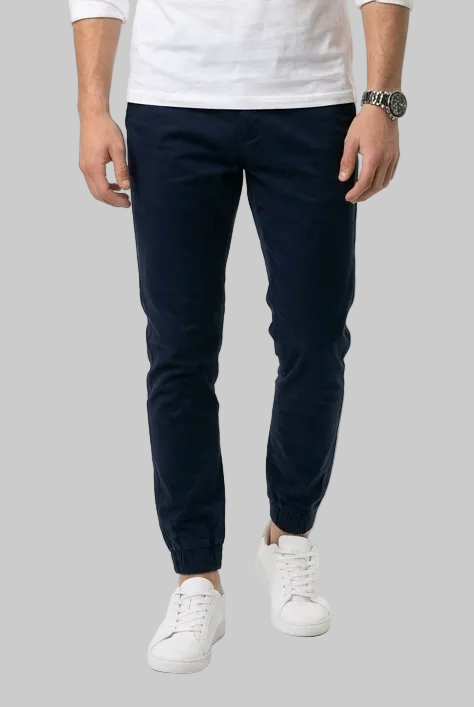 A man modeling a white long-sleeve crewneck shirt, dark navy golf pants, and white sneakers against a plain white studio background.