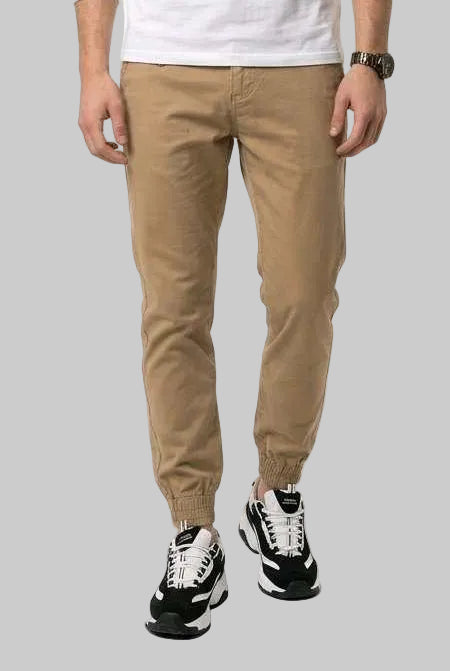 A man modeling a white long-sleeve crewneck t-shirt, tan golf chinos, and black-and-white sneakers against a plain white studio background.