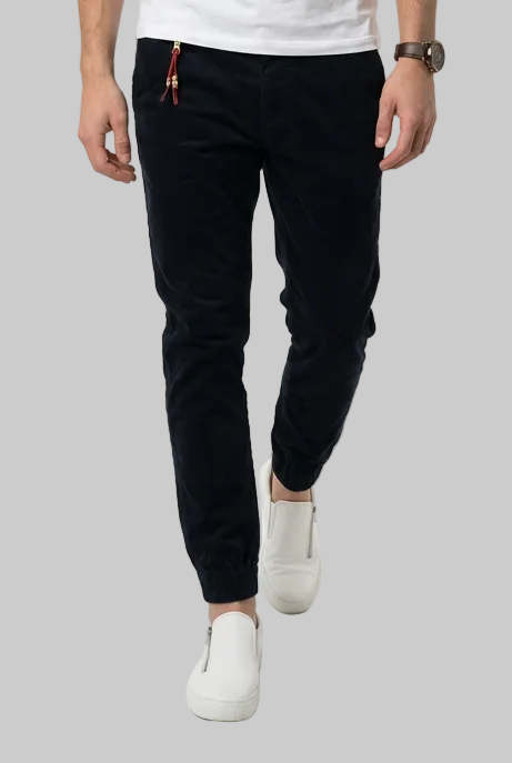 A man modeling a white crew-neck t-shirt and black slim-fit golf pants with white slip-on shoes, photographed against a seamless white studio background.