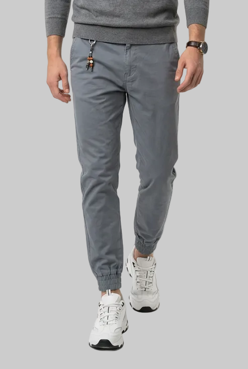 A man modeling a gray long-sleeve v-neck sweater, matching gray golf joggers, and white sneakers against a plain white studio background.