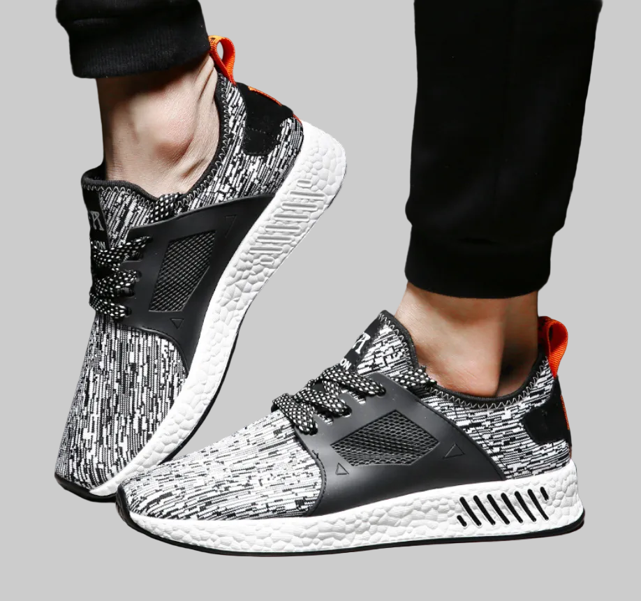 Black and white golf trainers with orange accents worn by a person on a white background